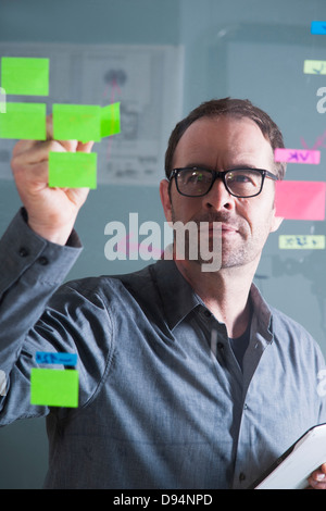 Businessman Looking at Self Adhesive Notes on Glass Board in Studio