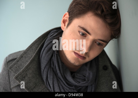 Head and Shoulder Portrait of Young Man wearing Grey Scarf and Jacket, Absorbed in Thought, Studio Shot on Grey Background Stock Photo