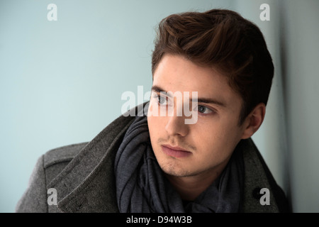 Head and Shoulder Portrait of Young Man wearing Grey Scarf and Jacket, Absorbed in Thought, Studio Shot on Grey Background Stock Photo