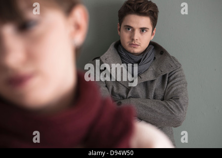 Portrait of Young Man Standing behind Young Woman, Looking at her Intensely, Studio Shot on Grey Background Stock Photo