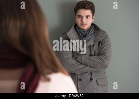 Portrait of Young Man Standing in front of Young Woman, Looking at her Intensely, Studio Shot on Grey Background Stock Photo