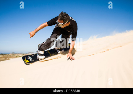 Adult man sandboarding on the dunes of Itapiruba Beach. Stock Photo