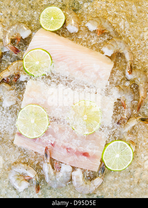 Vertical photo of fresh raw white fish, shrimp, lime slices and crushed ice on top with natural stone underneath as background Stock Photo
