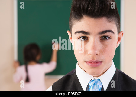 Portrait of Boy in Classroom with Girl in Background at Chalkboard Stock Photo