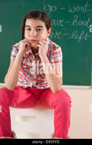 Portrait of Girl Sitting in Front of Chalkboard in Classroom Stock Photo