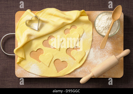 Overhead View of Hearts cut out of Cookie Dough with Rolling Pin, Wooden Spoon and Bowl of Flour Stock Photo
