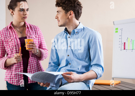 Young Businessman and Young Businesswoman Discussing Document in Office Stock Photo
