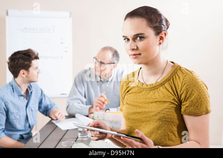 Portrait of Young Businesswoman holding Tablet with Colleagues Meeting in the Background Stock Photo