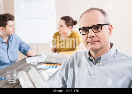 Portrait of Mature Businessman wearing Eyeglasses with Colleagues Meeting in the Background Stock Photo
