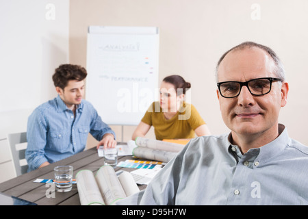 Portrait of Mature Businessman wearing Eyeglasses with Colleagues Meeting in the Background Stock Photo