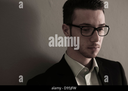 Close-up Portrait Young Man wearing Suit Jacket and Horn-rimmed Eyeglasses Looking Downward Absorbed in Thought Studio Shot Stock Photo