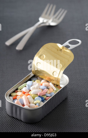 Variety of Pills in Opened Tin with Forks in Background, Studio Shot Stock Photo