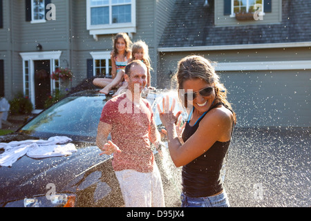 A family washes their car in the driveway of their home on a sunny summer afternoon in Portland, Oregon, USA