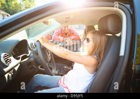 Young girl sitting in driver's seat car pretending be old enough drive as her smiling father watches on on sunny summer evening Stock Photo