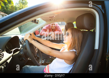 Young girl sitting in driver's seat car pretending be old enough drive as her smiling father watches on on sunny summer evening Stock Photo