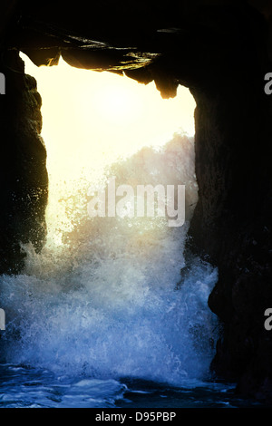 Waves break through the natural arch of a large rock formation at beach on Pacific ocean coast near Big Su, America USA Stock Photo