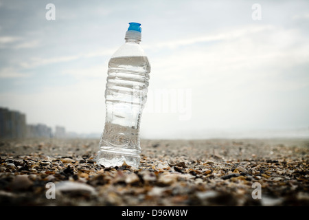 Low angle view of a single full water bottle sitting prominently among broken shells at the beach on an overcast day. Stock Photo