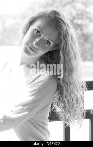 Beautiful young woman with long curly hair leans head back and smiles at camera Stock Photo