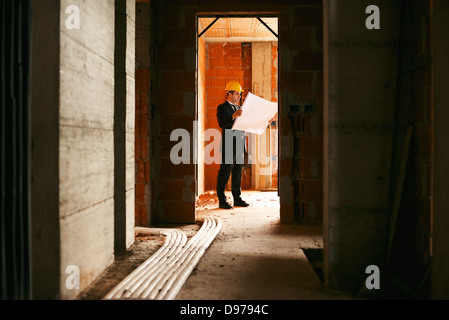 Engineer at work in construction site, standing in apartment building and looking at blueprints and plans Stock Photo