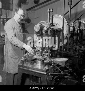 Historical 1950s. An engineer wearing a factory overall checks his machinery is working correctly. Stock Photo