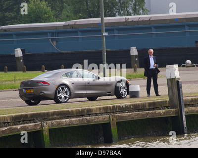 Fisker Karma electric sportscar parked in the port of Rotterdam with driver standing next to it Stock Photo