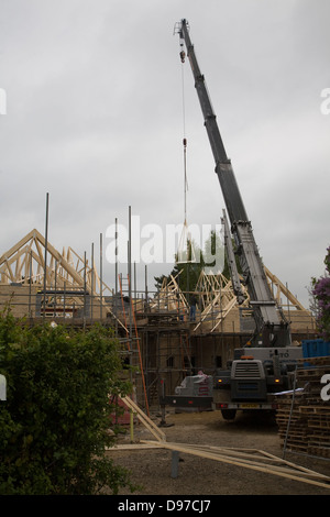 Crane lifting timber roof frame into place on building site, UK Stock Photo