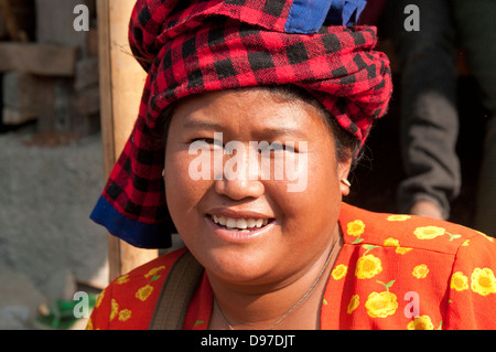 Woman wearing bright red checked headdress smiling at camera in a market Myanmar (Burma)