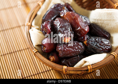 Dried date palm fruits or kurma, ramadan food which eaten in fasting month. Pile of fresh dried date fruits in bamboo basket. Stock Photo