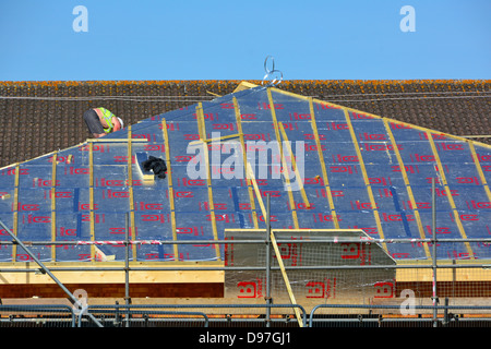 Scaffolding on building construction site & workman fixing foil backed energy saving foam insulation sloping roof on school extension Essex England UK