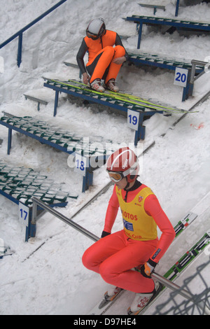 Ski Jumper at top of jump preparing to set-off. Another jumper waits and adjusts boots. Stock Photo