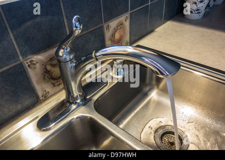 Kitchen faucet with running water into stainless steel double sinks. Closeup. USA. Stock Photo