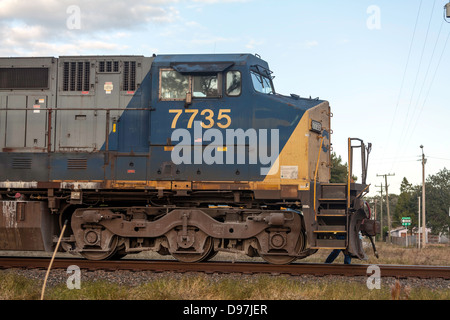 CSX engine 7735 pulling a freight train through a railroad crossing in Hawthorne, Florida. The flagman runs beside the engine. Stock Photo