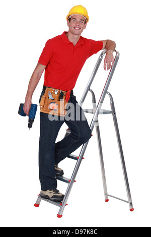 Young tradesman standing on a stepladder and holding a screw gun Stock Photo
