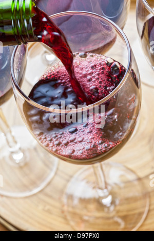 Red wine being poured into a glass, one of several on a tray. Stock Photo