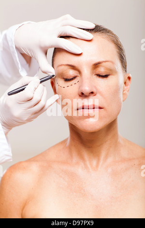 doctor draw correction lines on senior womans face before plastic surgery Stock Photo