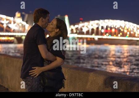 Loving Caucasian couple kissing on a granite embankment opposite Bolsheokhtinsky Bridge in St. Petersburg. White nights period Stock Photo