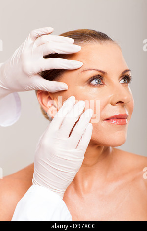 doctor doing skin check on mid age woman face over white background Stock Photo