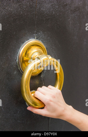 Fair, small female hand holding a golden door knocker ring on a door in Modena, Emilia-Romagna, Italy Stock Photo