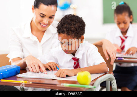 caring elementary school teacher helping student in classroom Stock Photo
