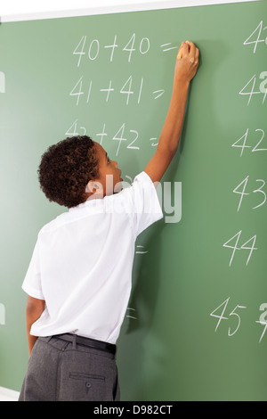 elementary school student writing maths answer on chalkboard Stock Photo