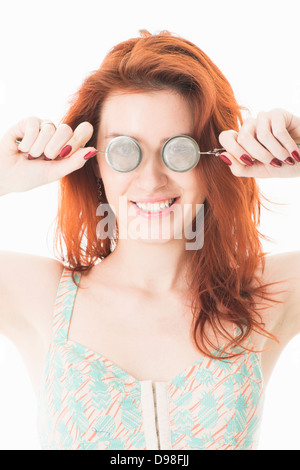 Playful young red haired woman in her 20s holding tea infusers in front of her eyes Stock Photo