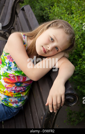 beautiful young girl is sitting on the bench at park in summer Stock Photo