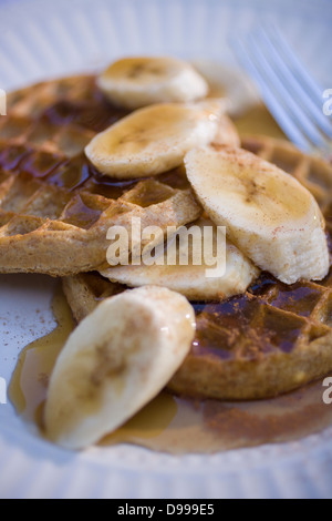 two whole wheat waffles maple syrup sliced bananas on a round plate Stock Photo