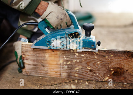 Man with protection gloves using an electric scraper to plane a plank Stock Photo