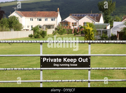 Dog running loose, private keep out sign on a gate, with houses in the distance, June 2013 Stock Photo