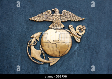 Insignia of the United States Marine Corps in golden burnished metal on a dark blue-gray wall. Stock Photo