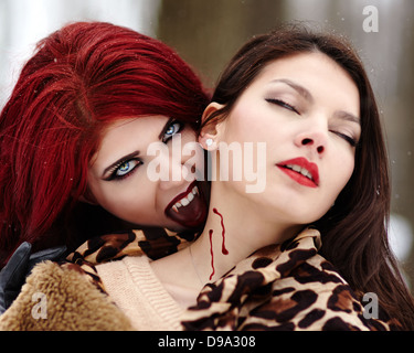 Closeup of a redheaded vampire biting innocent girl Stock Photo