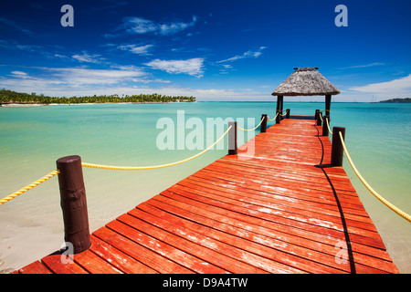 Wooden red jetty extending to tropical green lagoon Stock Photo