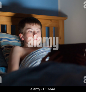 A 13 year old teenage boy using a tablet on the internet in bed Stock Photo