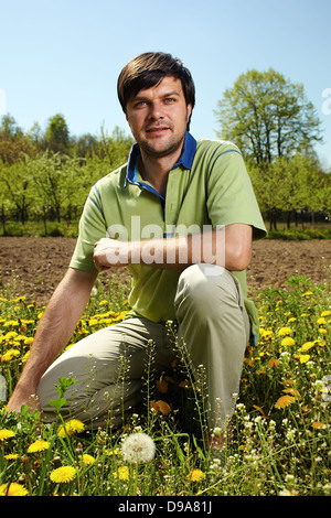 Young farmer knelt near his land in a sunny day Stock Photo